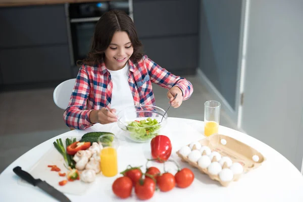Söt tonåring flicka förbereda sallad för frukost i köket ser glad — Stockfoto