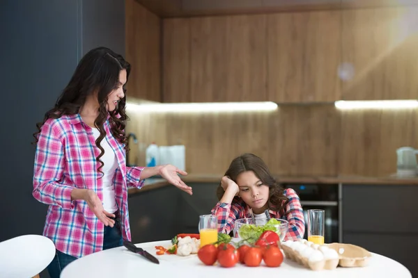 Ung vacker kvinna som har ett gräl med sin tonåring dotter under frukosttillagning i köket — Stockfoto