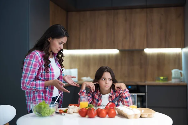 Ung vacker kvinna som har bråkat med sin tonåring dotter under matlagning i köket ser upprörd — Stockfoto