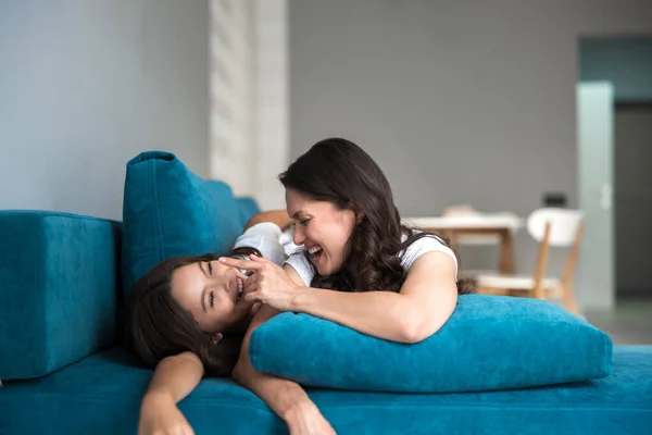Красивая молодая мать и ее симпатичная дочь-подросток веселятся на диване, улыбаясь и скорбя — стоковое фото
