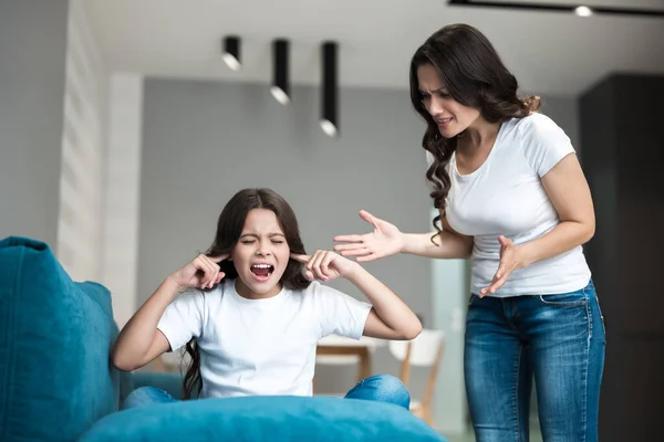 Jeune belle femme ayant une dispute avec sa fille adolescente criant fort dans le salon enfant assis avec ses oreilles fermées — Photo