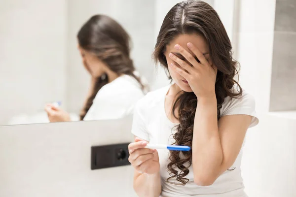 Jeune femme brune s'assoit sur le bol de toilette tenant test de grossesse à la recherche bouleversée — Photo