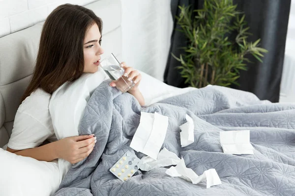 Joven enferma sentada en la cama tomando pastillas usando toallas de papel por la mañana —  Fotos de Stock