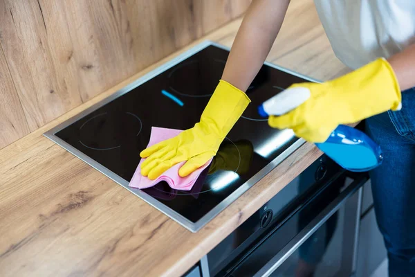 Process of cleaning. womans hands in yellow gloves using detergent spray wiping dust off from the kitchen hob with a rag — Stock Photo, Image