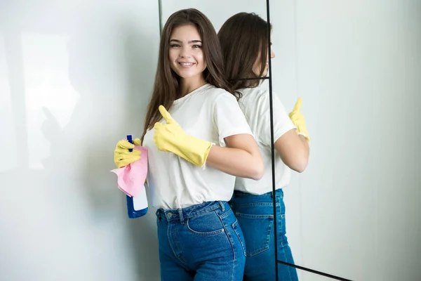 Beautiful young smiling woman in yellow gloves with detergent spray and rag in her hand showing ok sign — Stock Photo, Image