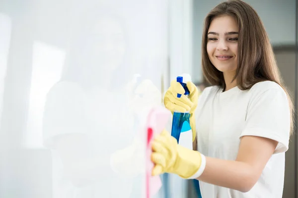 Cute young woman in yellow gloves spraying detergent spray while wiping dust off from the kitchen wall with a rag thoroughly — Stock Photo, Image