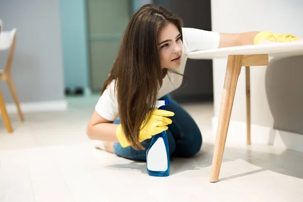 Linda joven con guantes amarillos con spray detergente en la mano limpiando el polvo de la silla de la cocina con un trapo a fondo — Foto de Stock