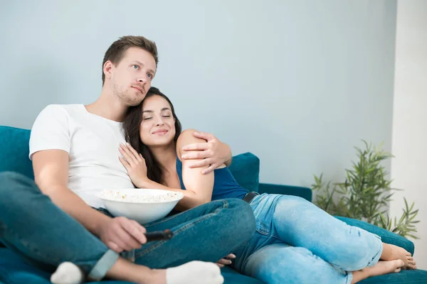 Jong paar mooi brunette vrouw en knappe man kijken film op de bank eten pop maïs knuffelen gezellige levensstijl — Stockfoto