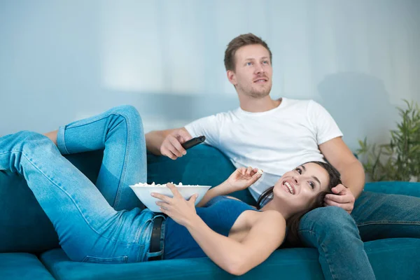 Jeune couple mignon belle femme brune allongé sur beau mans jambe tout en regardant le film sur le canapé et en mangeant pop-corn doux moments — Photo