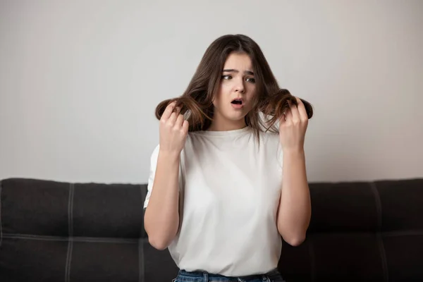 brunette young woman with damaged long hair and split ends looks desparate and unhappy with her hairstyle, bad hair day concept.