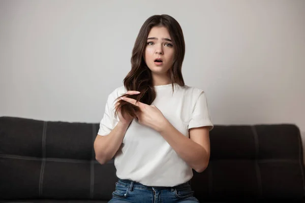 brunette young woman with damaged long hair and split ends looks desparate and upset with her hairstyle, bad hair day concept.