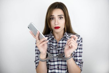 brunette young woman holds smartphone in her hands, having handcuffs on , virtual reality concept, social media addiction, nomophobia, isolated white background. clipart