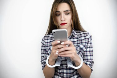 Esmer, konsantre genç bir kadın elinde akıllı telefon, kelepçeliyken mesajlar, sanal gerçeklik konsepti, sosyal medya bağımlılığı, nomofobi, izole edilmiş beyaz arka plan.