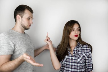young couple handsome man and beautiful woman quarrelling on isolated white background, she shows him fuck off sign , relationships problem concept.