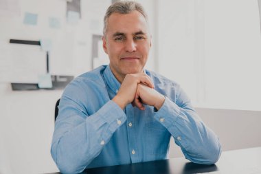 Yakışıklı, başarılı, gri saçlı iş adamı modern parlak ofisinde oturmuş iş projesi üzerinde çalışıyor. Para motivasyon kavramı oluşturuyor..