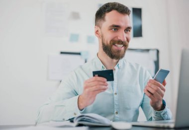 Yakışıklı, gülümseyen sakallı iş adamı elinde banka kartıyla ofiste oturuyor. Akıllı telefon iş projesinde çalışırken heyecanlı görünüyor. Para motivasyon kavramı oluşturuyor..