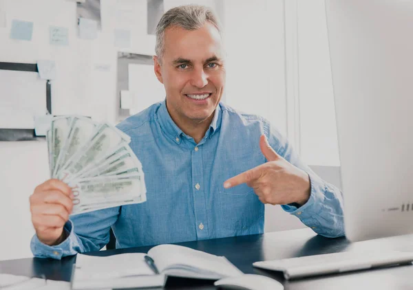 Guapo Hombre Pelo Gris Sienta Oficina Sosteniendo Efectivo Mano Como — Foto de Stock