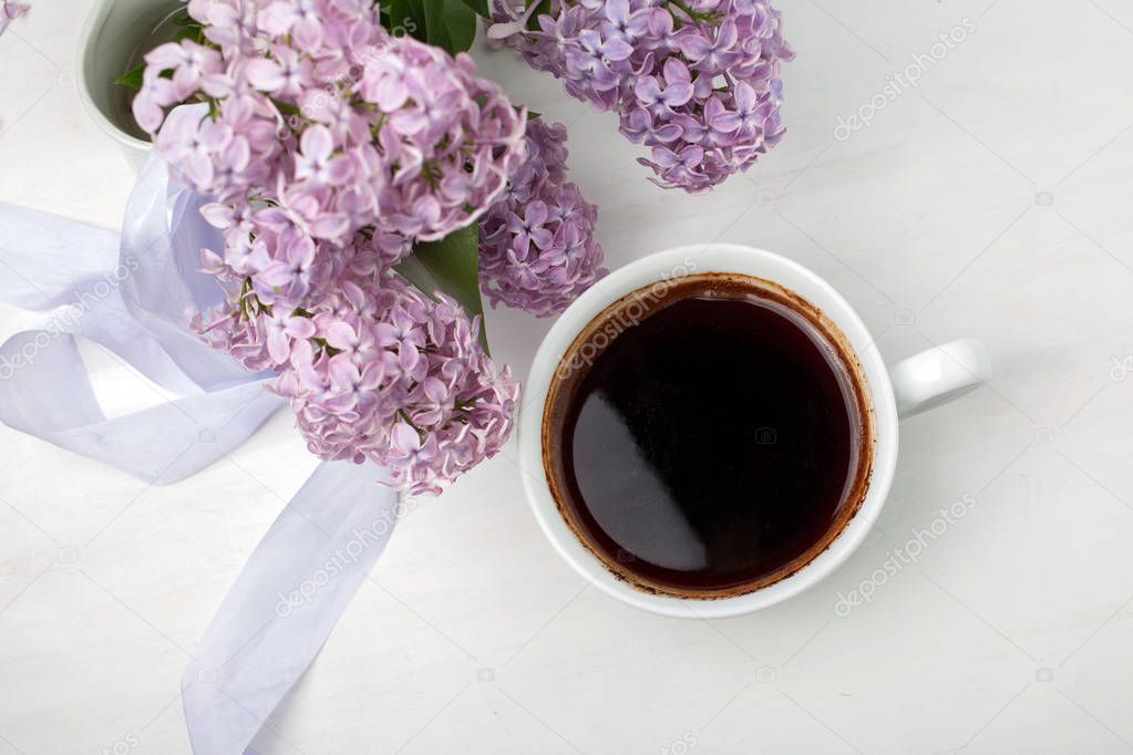 Floral composition made of beautiful purple lilac on white wooden background with cup of coffee.