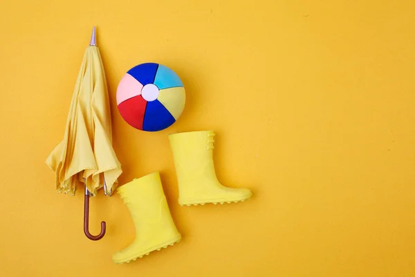 Un par de botas de lluvia amarillas y un paraguas y una bola en un amarillo — Foto de Stock