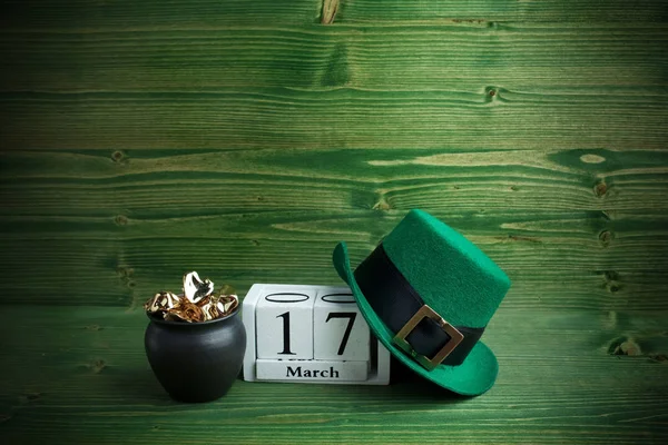 3月17日圣帕特里克节的白色方块日历, 带有小妖精帽和金罐, 以绿色木制为背景. — 图库照片