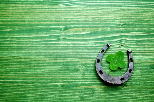 Quadrifoglio e scarpa da cavallo su fondo verde in legno. San Patrizio giorno — Foto Stock