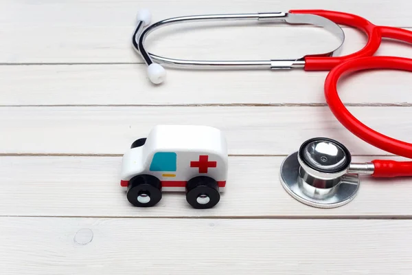 Ambulans servicekoncept. Ambulans fordon leksak nära stetoskop på vit trä bakgrund — Stockfoto