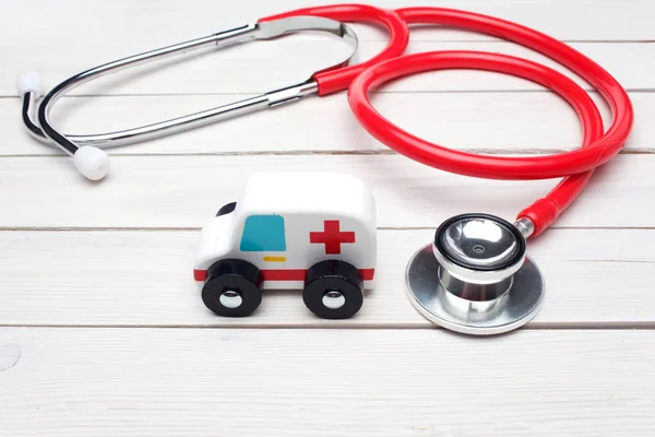 Ambulans servicekoncept. Ambulans fordon leksak nära stetoskop på vit trä bakgrund — Stockfoto