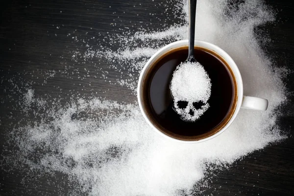 Unhealthy white sugar concept. Scull spoon with sugar and cup of black coffee on wooden background — Stock Photo, Image