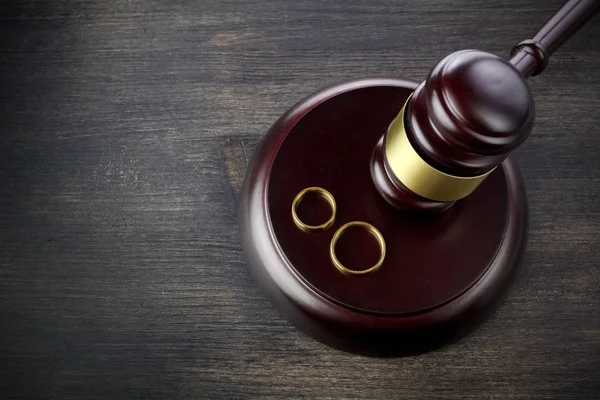 Los anillos de boda martillo de un juez sobre un fondo de madera oscura. Procedimientos de divorcio — Foto de Stock