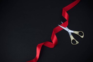 Grand opening. Top view of gold scissors cutting red ribbon on black background. clipart