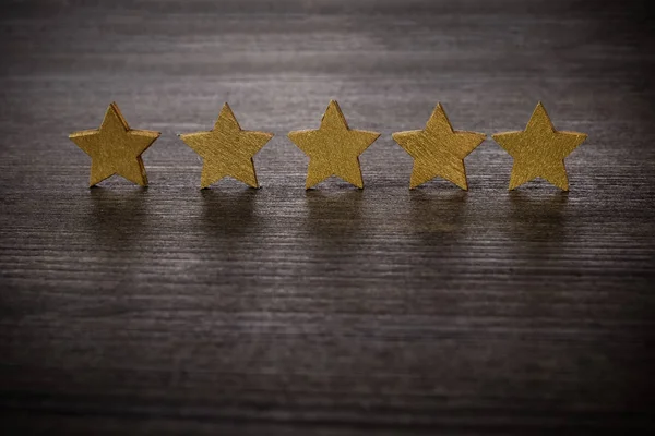 five golden stars on wooden background, top rating concept