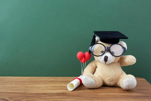 Ведмедик Тедді з випускним капелюхом та дипломом перед зеленою дошкою. Концепція школи — стокове фото