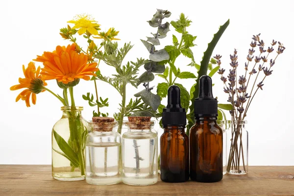 Aceites esenciales con hierbas y flores sobre mesa de madera — Foto de Stock