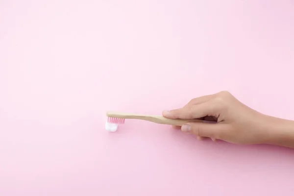 Mano de niño con cepillo de dientes y diente plático blanco sobre fondo rosa — Foto de Stock