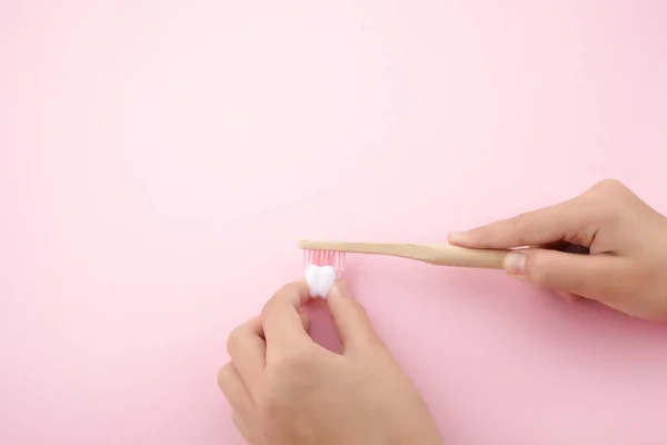 Mano de niño con cepillo de dientes y diente plático blanco sobre fondo rosa — Foto de Stock