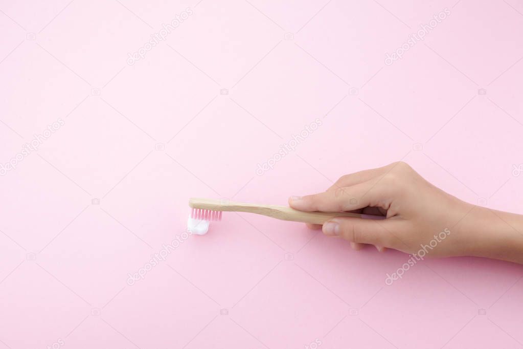 childs hand with toothbrush and white platic tooth on pink background