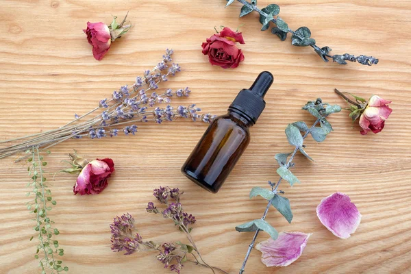 Aceite esencial con hierbas y flores sobre mesa de madera — Foto de Stock