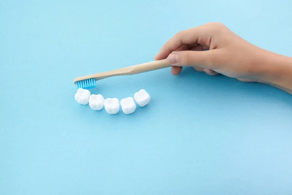 Mavi arka plan üzerinde diş fırçası ve beyaz platik diş ile çocuk el — Stok fotoğraf