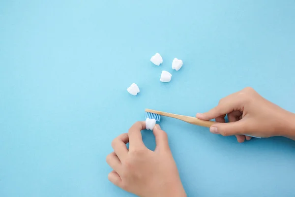 Childs hand met tandenborstel en witte platic tand op blauwe achtergrond — Stockfoto
