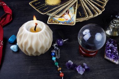 Tahta masanın üzerinde tarot kartları, sihirli taşlar ve mumlarla natürmort. Falcılık seansı veya sihirli ritüel.