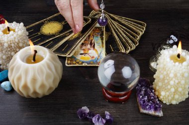 Tahta masanın üzerinde tarot kartları, sihirli taşlar ve mumlarla natürmort. Falcılık seansı veya sihirli ritüel.