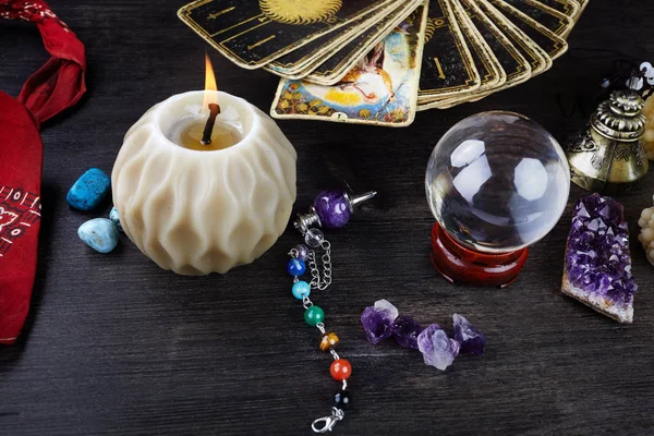 Tahta masanın üzerinde tarot kartları, sihirli taşlar ve mumlarla natürmort. Falcılık seansı veya sihirli ritüel.