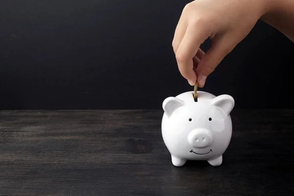 Business o concetto di risparmio finanziario con mano mettendo moneta in salvadanaio bianco su tavolo di legno scuro — Foto Stock