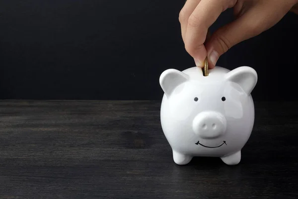 Conceito de economia de negócios ou finanças com a mão colocando moeda no banco piggy branco na mesa de madeira escura — Fotografia de Stock