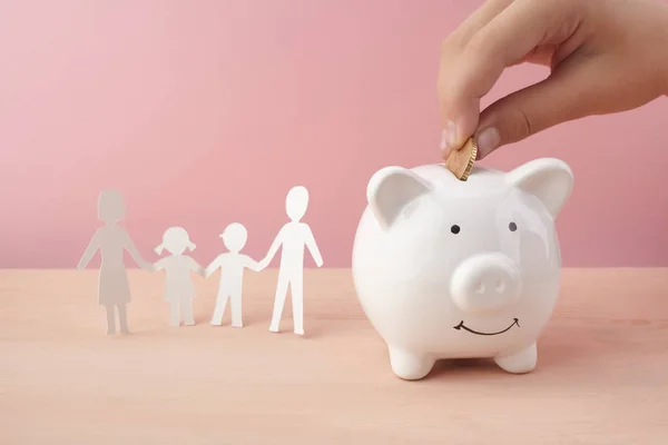 Concepto de ahorro familiar con alcancía y papel de familia cortado sobre fondo rosa —  Fotos de Stock