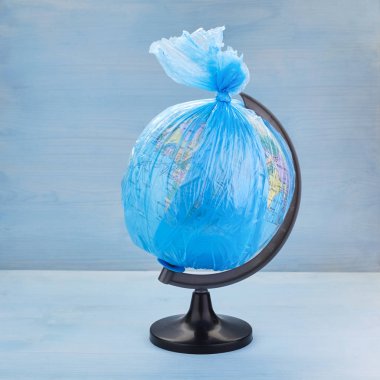 Dünya gezegeninin Küre mavi ahşap arka plan üzerinde bir çöp plastik torba giymiş