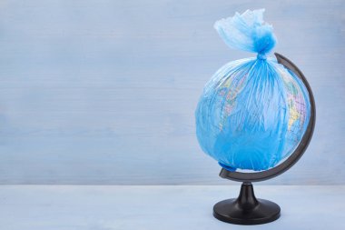 Dünya gezegeninin Küre mavi ahşap arka plan üzerinde bir çöp plastik torba giymiş