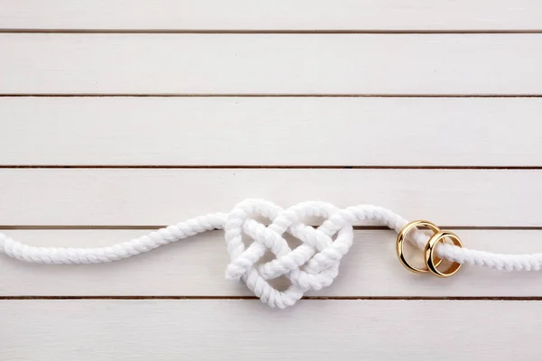 Heart shaped rope and a double gold ring on white wooden background — Stock Photo, Image