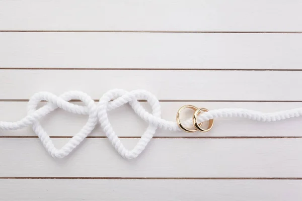 Cuerda en forma de corazón y doble anillo de oro sobre fondo de madera blanca — Foto de Stock