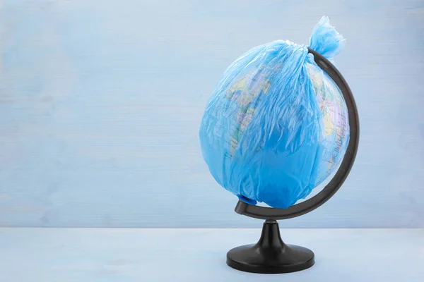 Globe of planet Earth dressed in a garbage plastic bag on blue wooden background